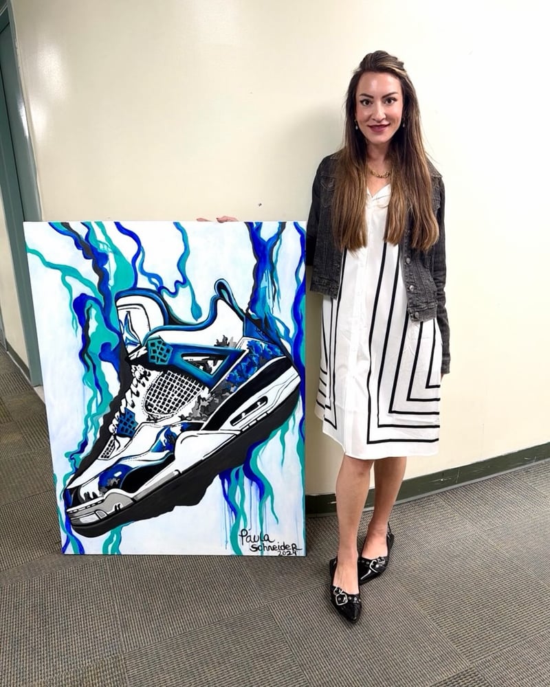 Paula standing beside one of her finished canvases — a painted sneaker wrapped in blue drips